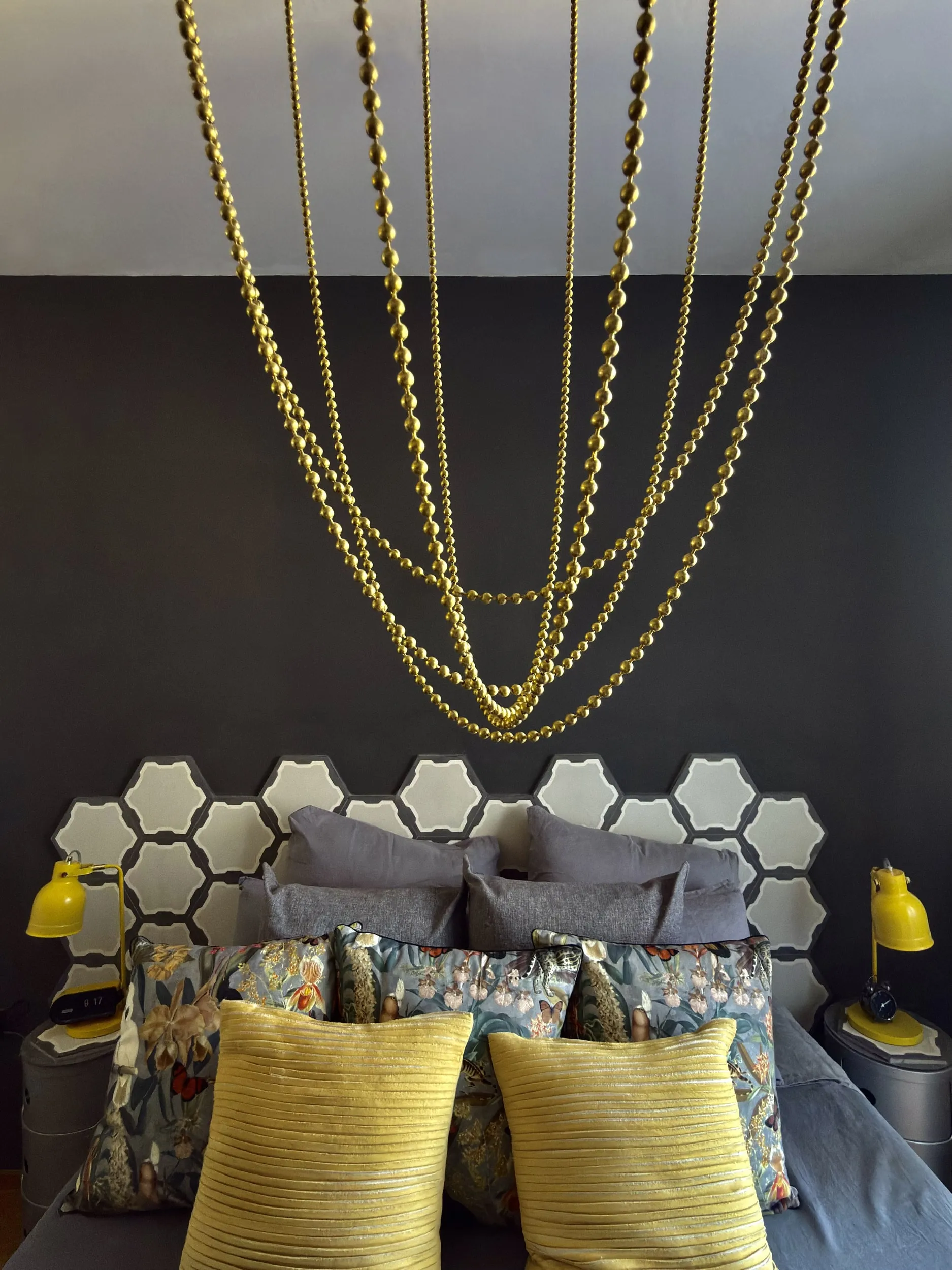 A black bedroom wall, brass bead chains above a honeycomb headboard