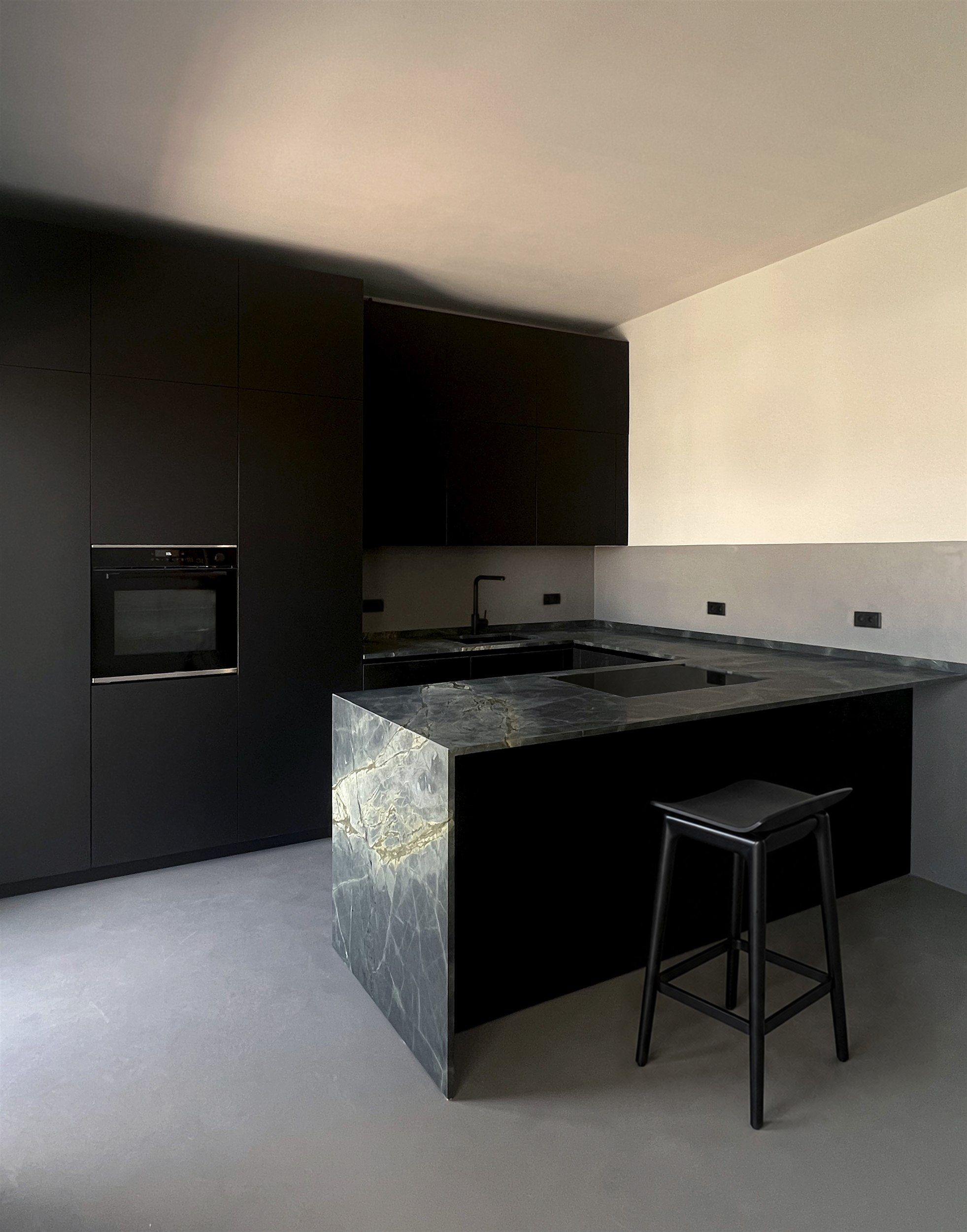 A matte black kitchen with a dark marble island in a white room
