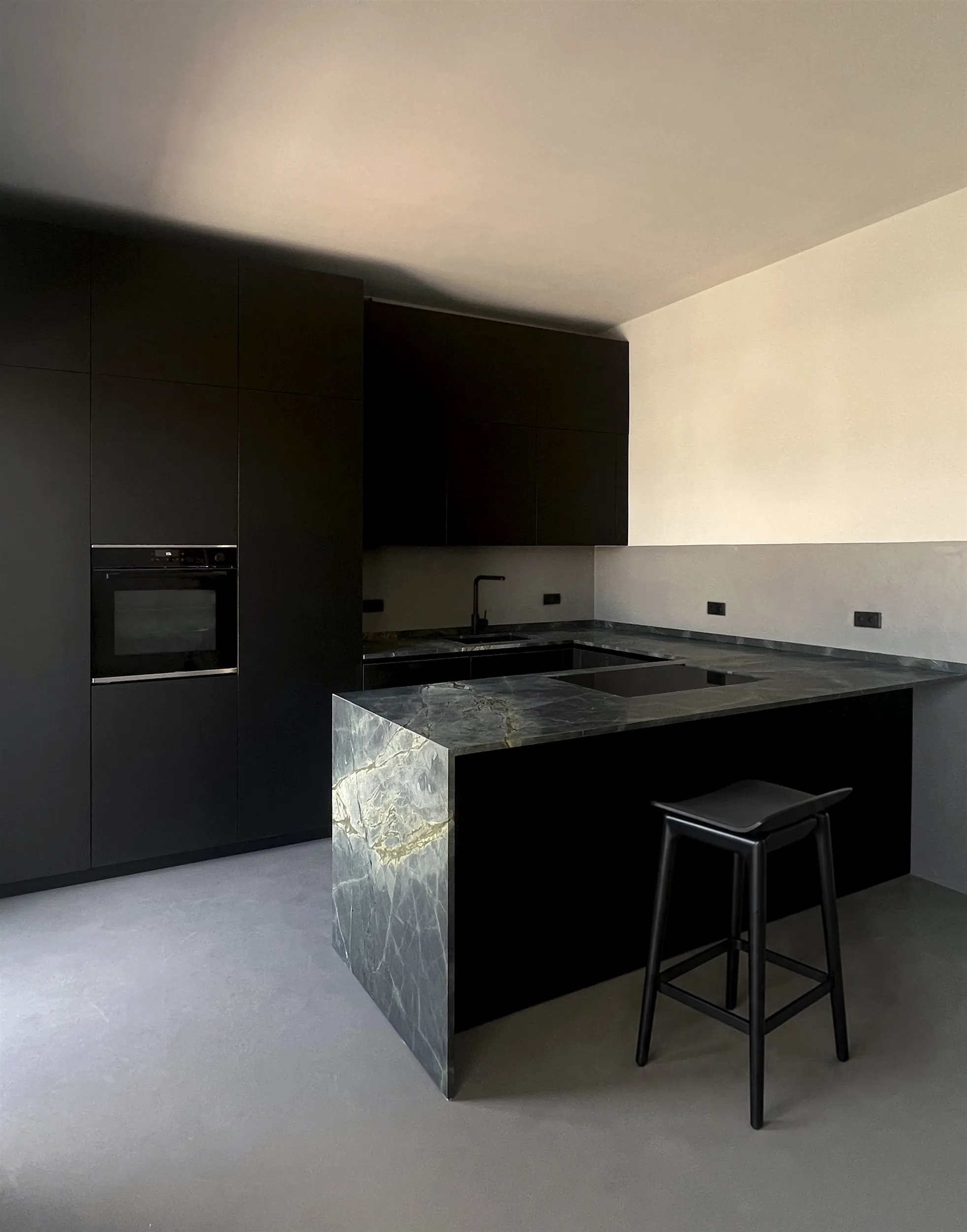 A matte black kitchen with a dark marble island in a white room