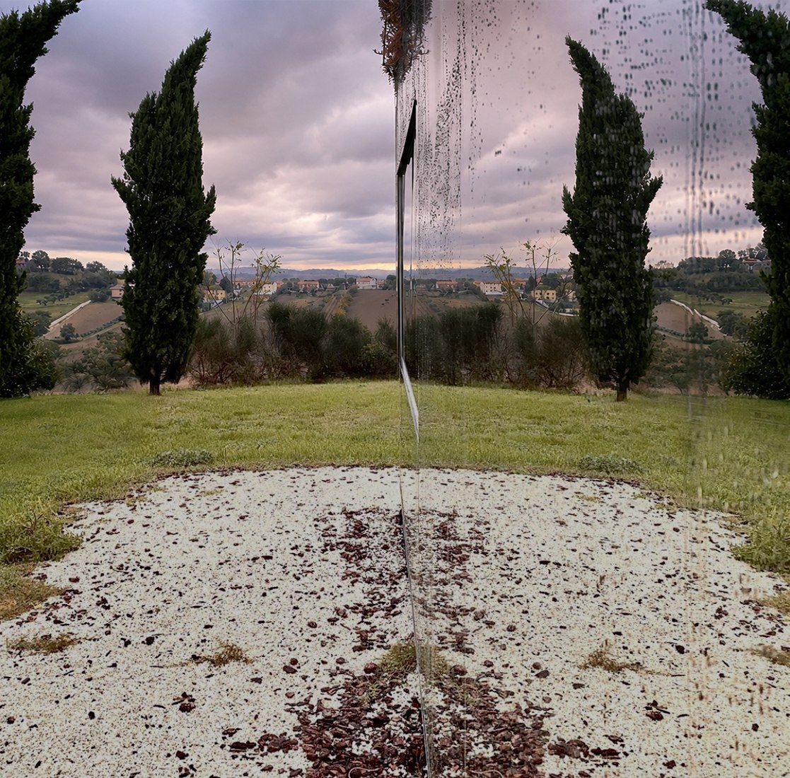 A rain-streaked mirror doubling cypresses and hills