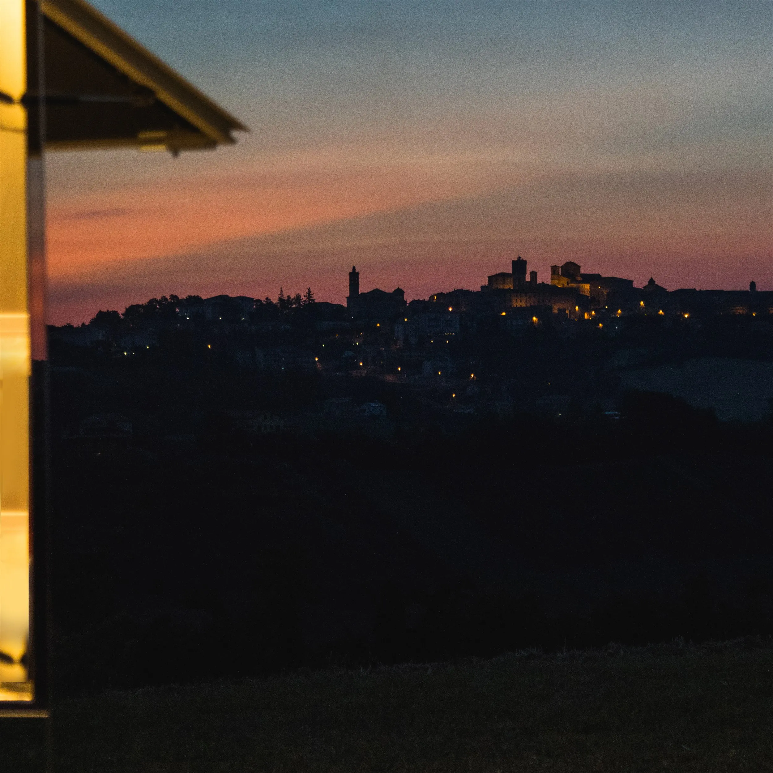 The lit edge of the mirrored bar against a hilltop village at dusk