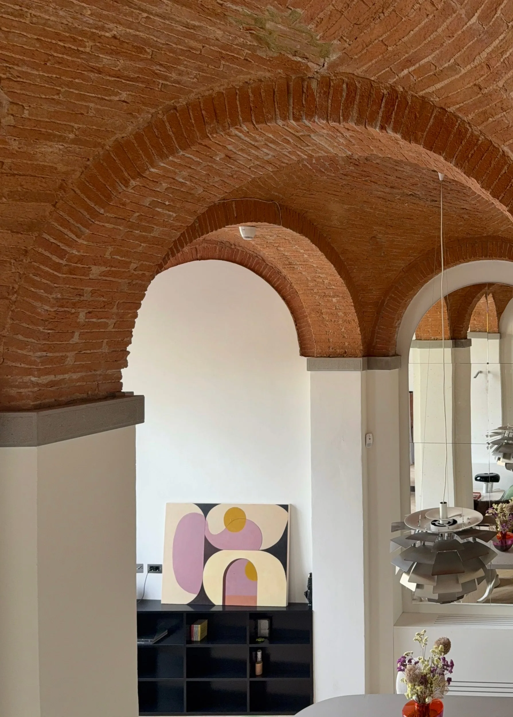 Brick vaults and, on the right, a mirrored wall doubling the arch and the lamp
