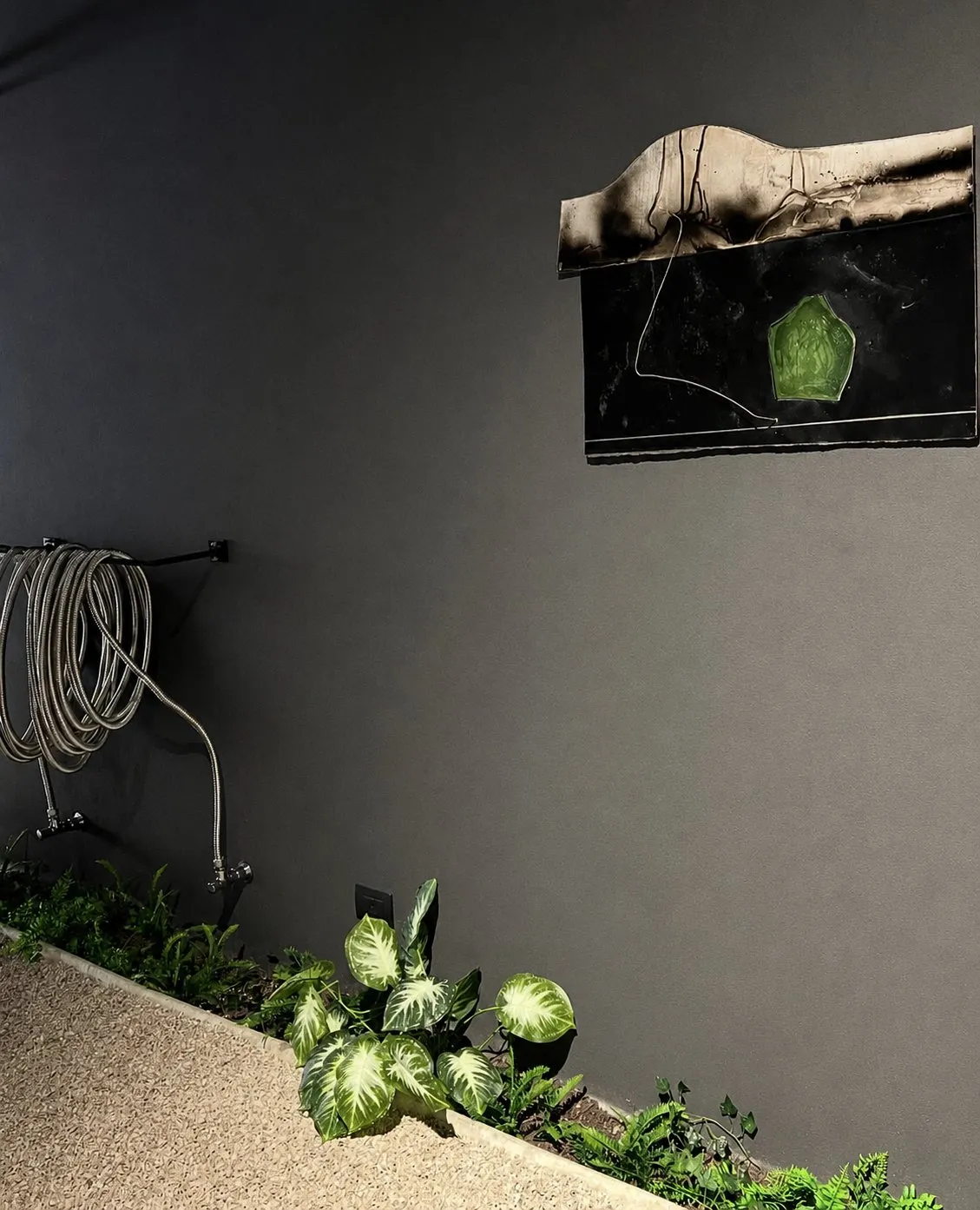 A wall relief in blackened metal with a green glass inset, hung above the coiled radiator and the planted border