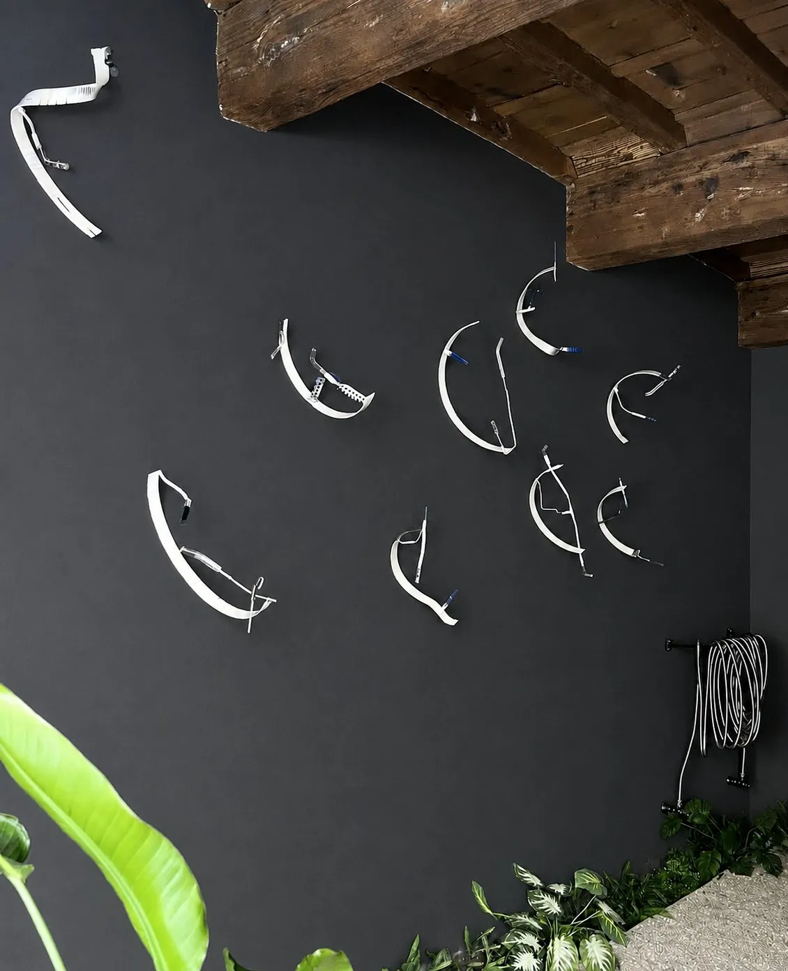 Nine white ribbon sculptures scattered across the black wall, under the beamed ceiling