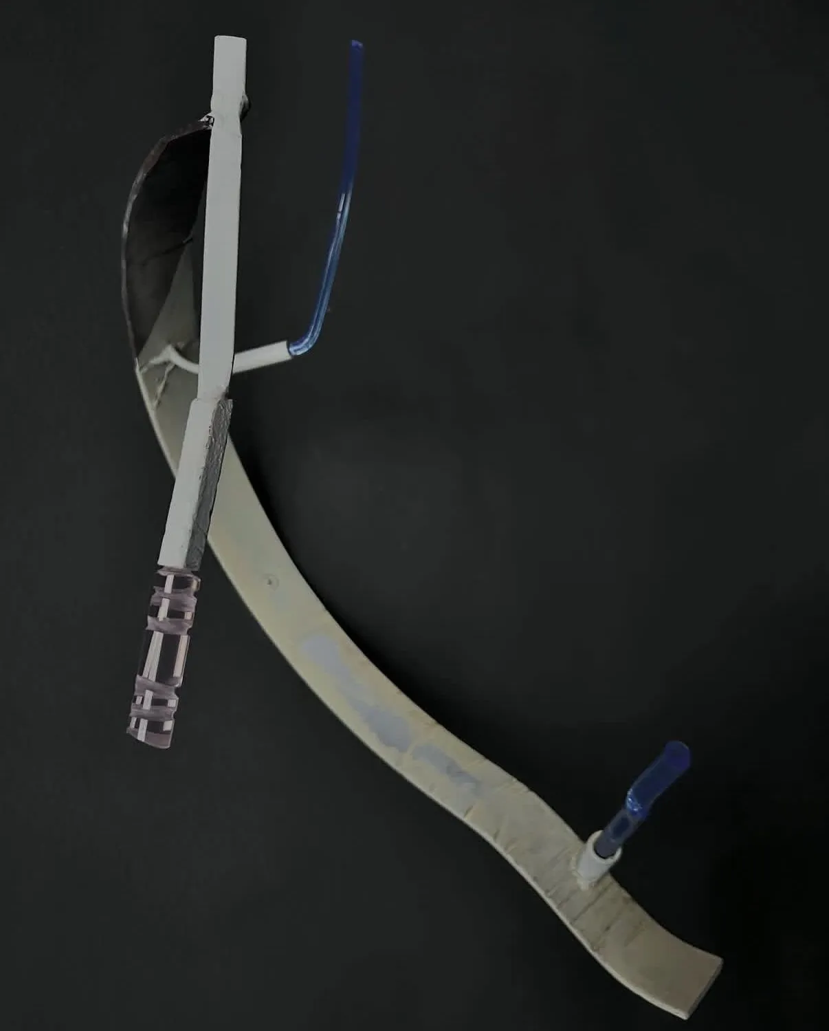 One sculpture close up: a pale curved blade crossed by a white bar and two blue grafts