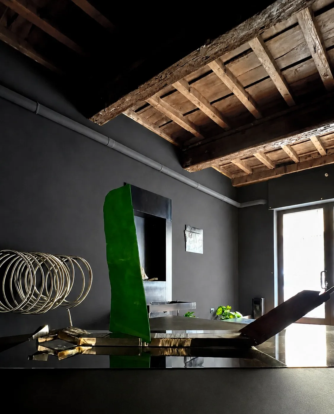 A tall green sculpture on a mirroring metal table, daylight from the glazed door behind it