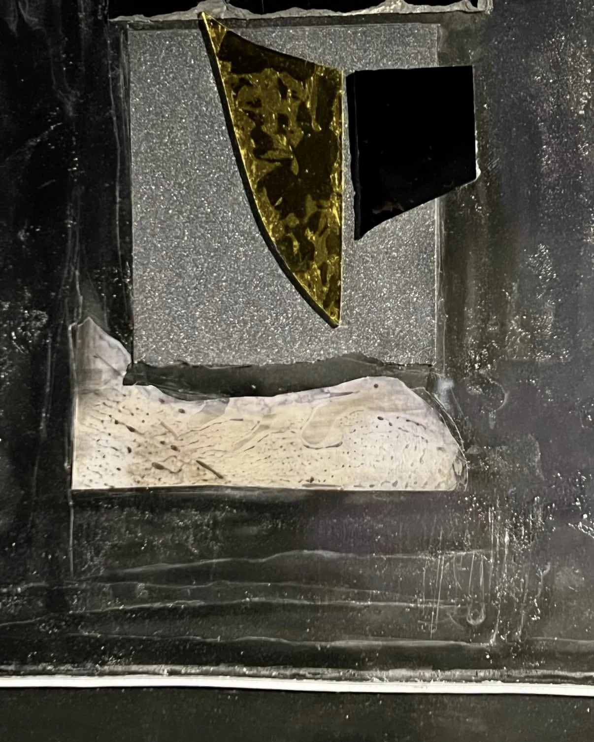 A relief close up: a gilded wedge, a black square and a scratched white field on tarred ground
