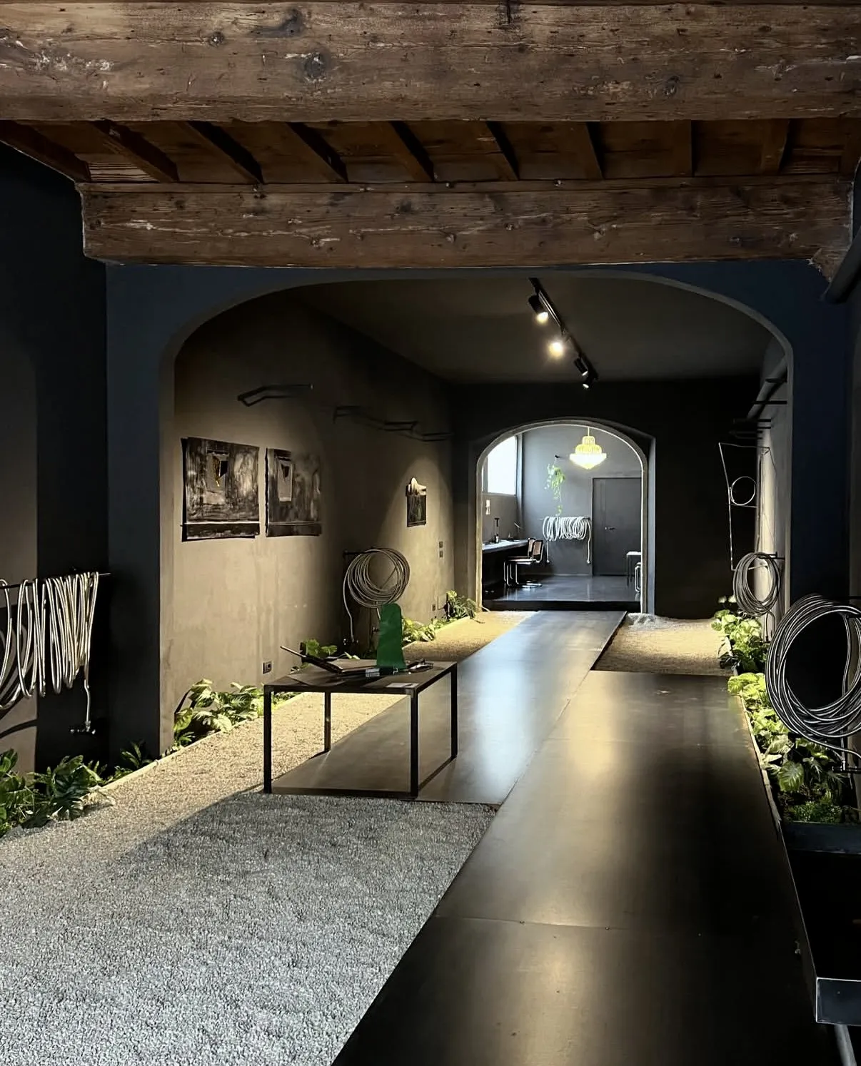 The full run of the atelier: the iron walkway between the gravel beds, works on the walls, the green sculpture halfway down