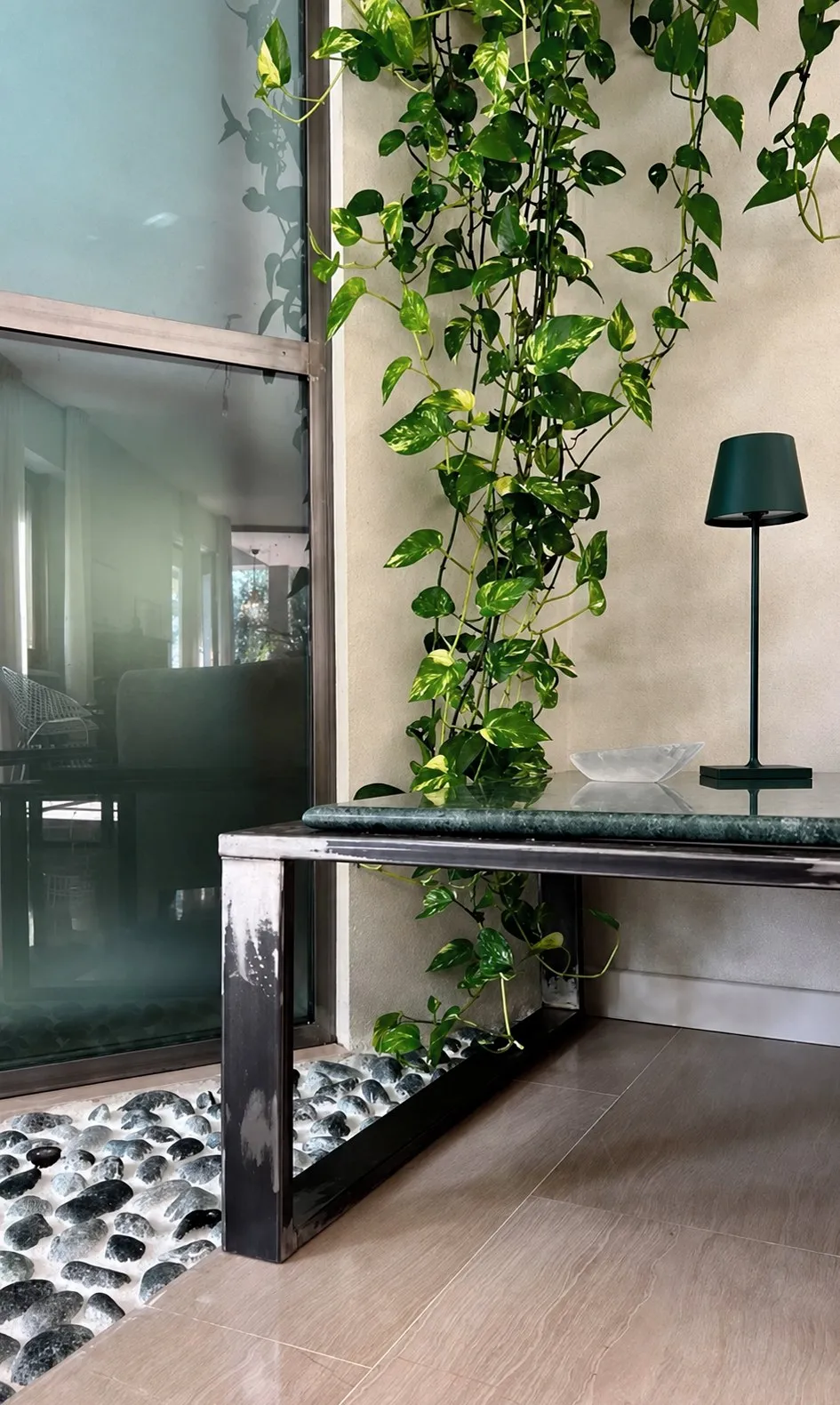 Pothos falling on a green marble console, pebbles at the glass wall